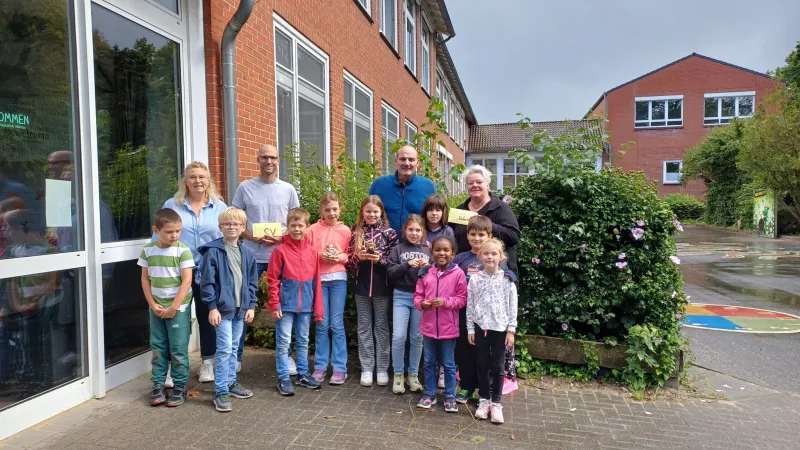 Die Kinder der Bienen-AG mit Lehrkräften und Vorstandsmitgliedern vor dem Schuleingang, zwei von ihnen halten die Umschläge für SV und Förderverein.