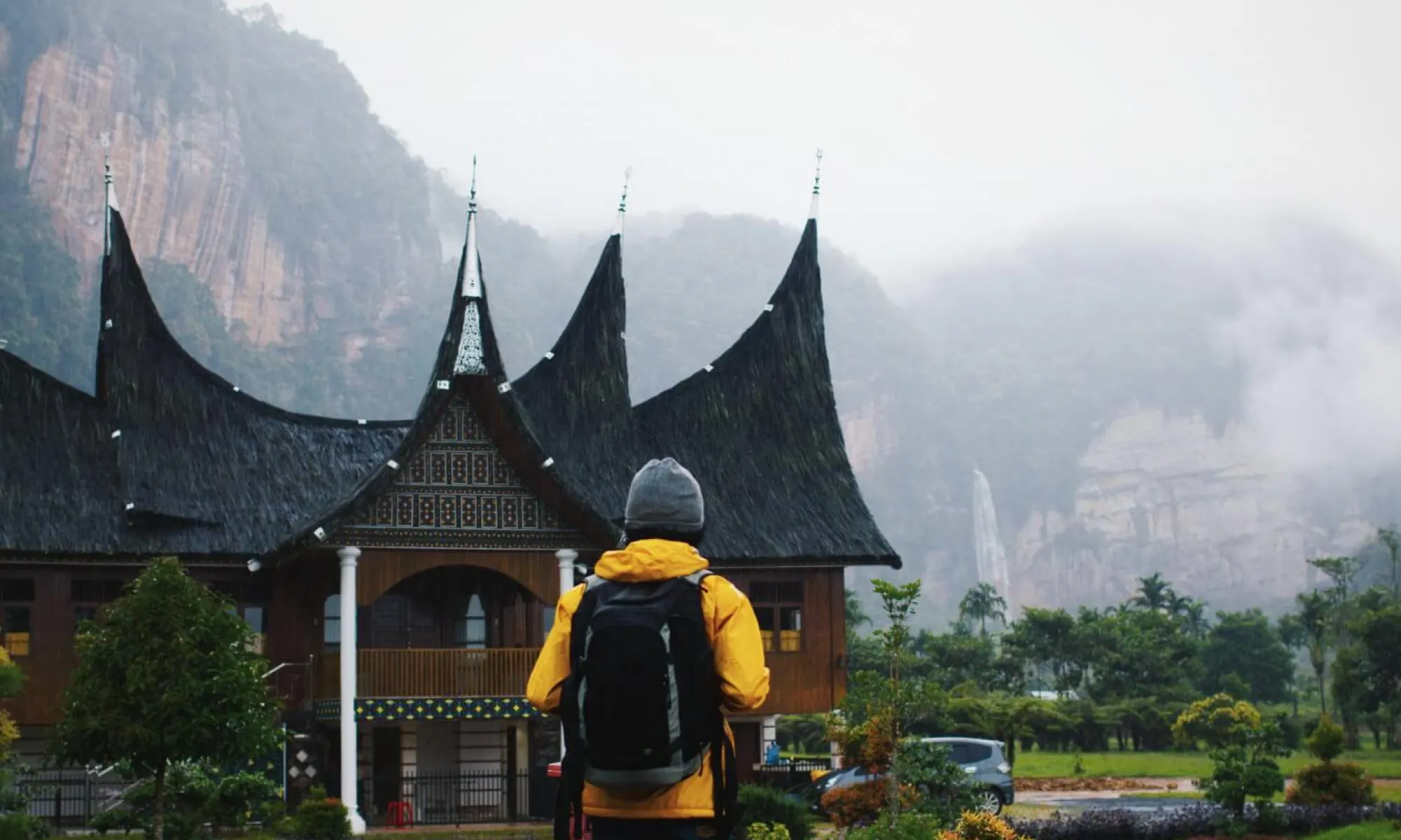 A hiker stands in front of an old asian building. Misty mountains in the background.