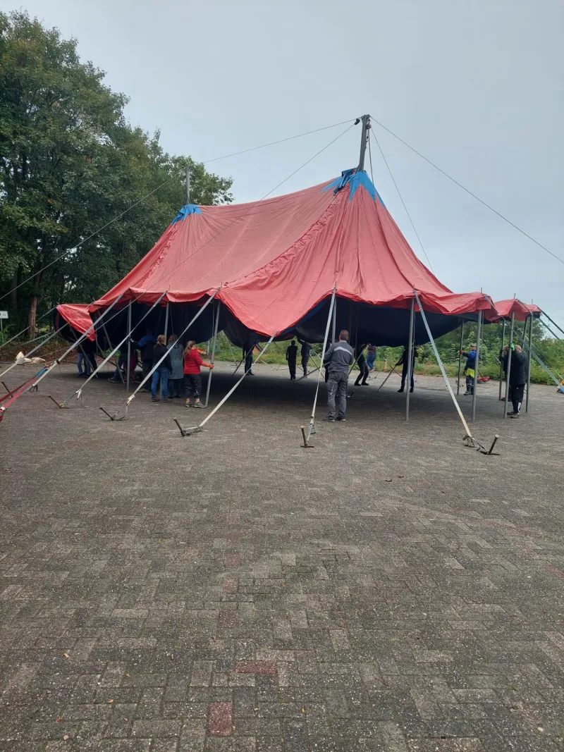Helferinnen und Helfer richten das rot-blaue Zirkuszelt auf dem gepflasterten Platz am Mühlenberg auf.