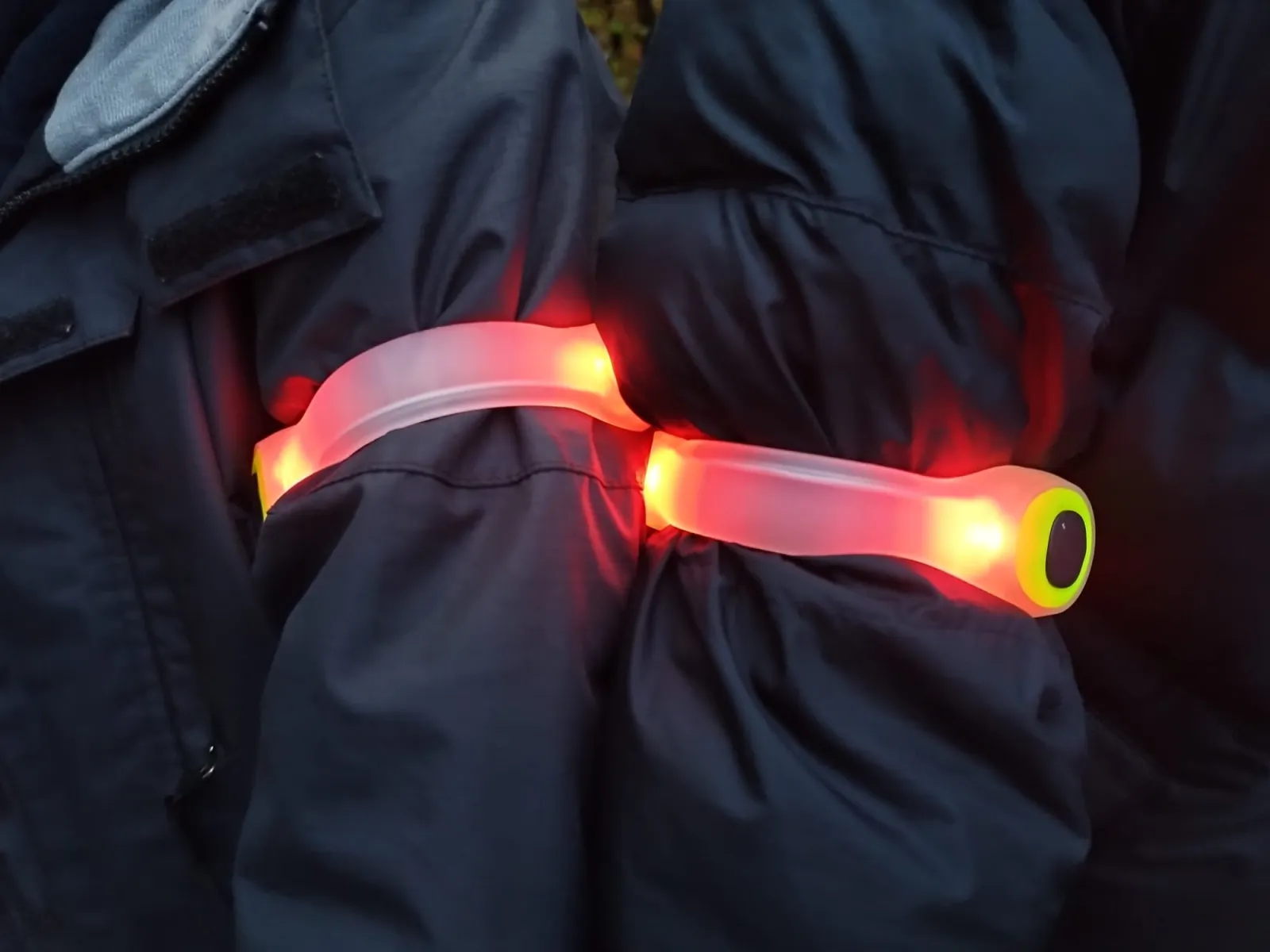 Zwei rot leuchtende LED-Armbänder an den dunklen Jacken zweier Kinder in der Dämmerung.